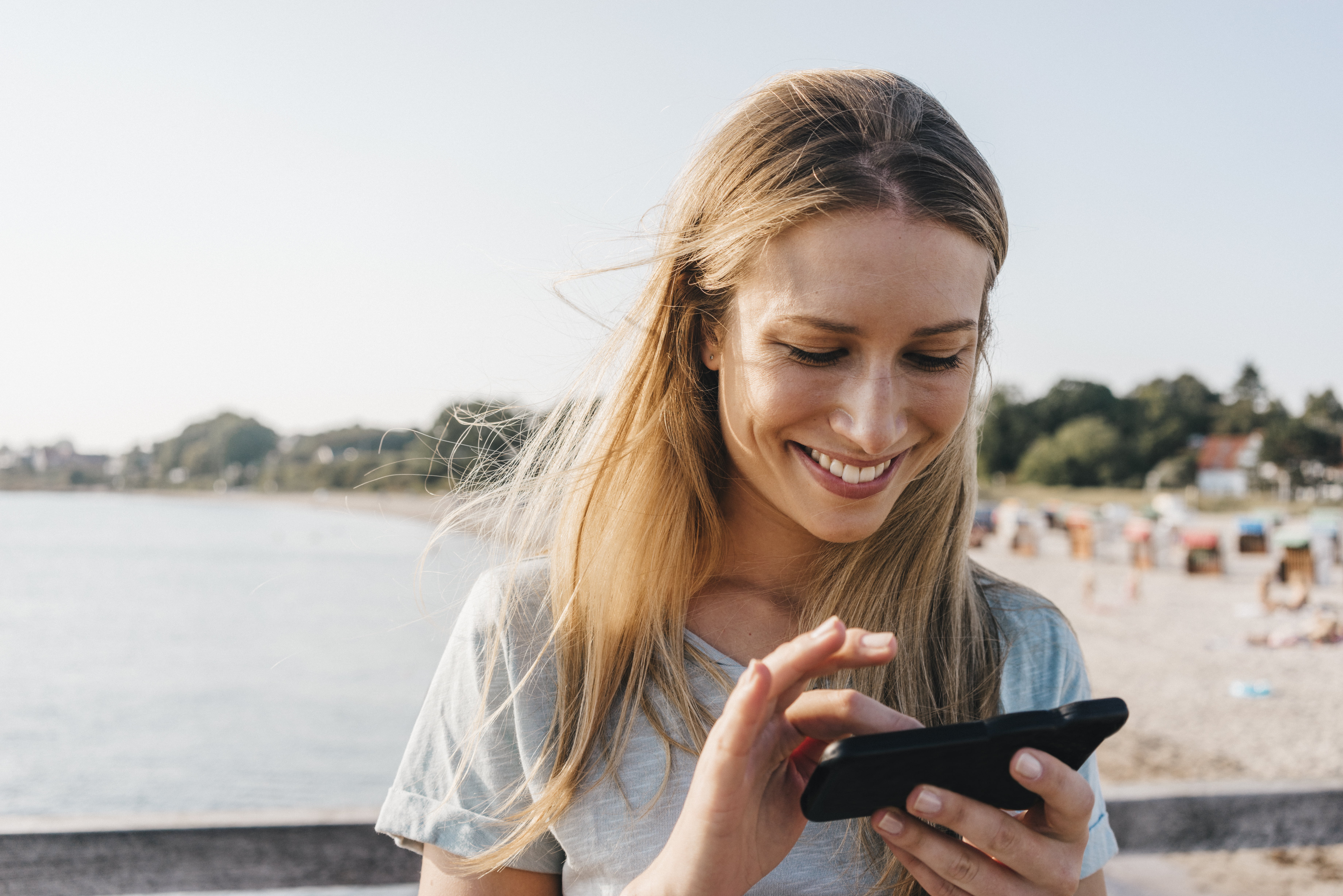 Kvinne på stranden ser på telefonen sin