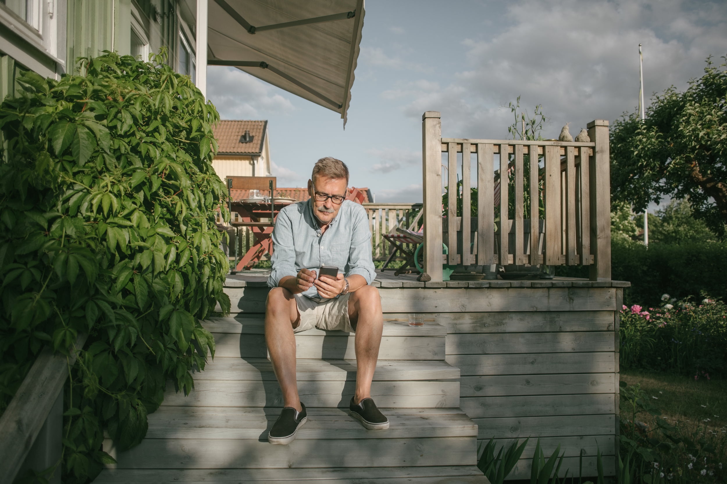 Eldre mann med mobil som sitter på trappen til verandaen