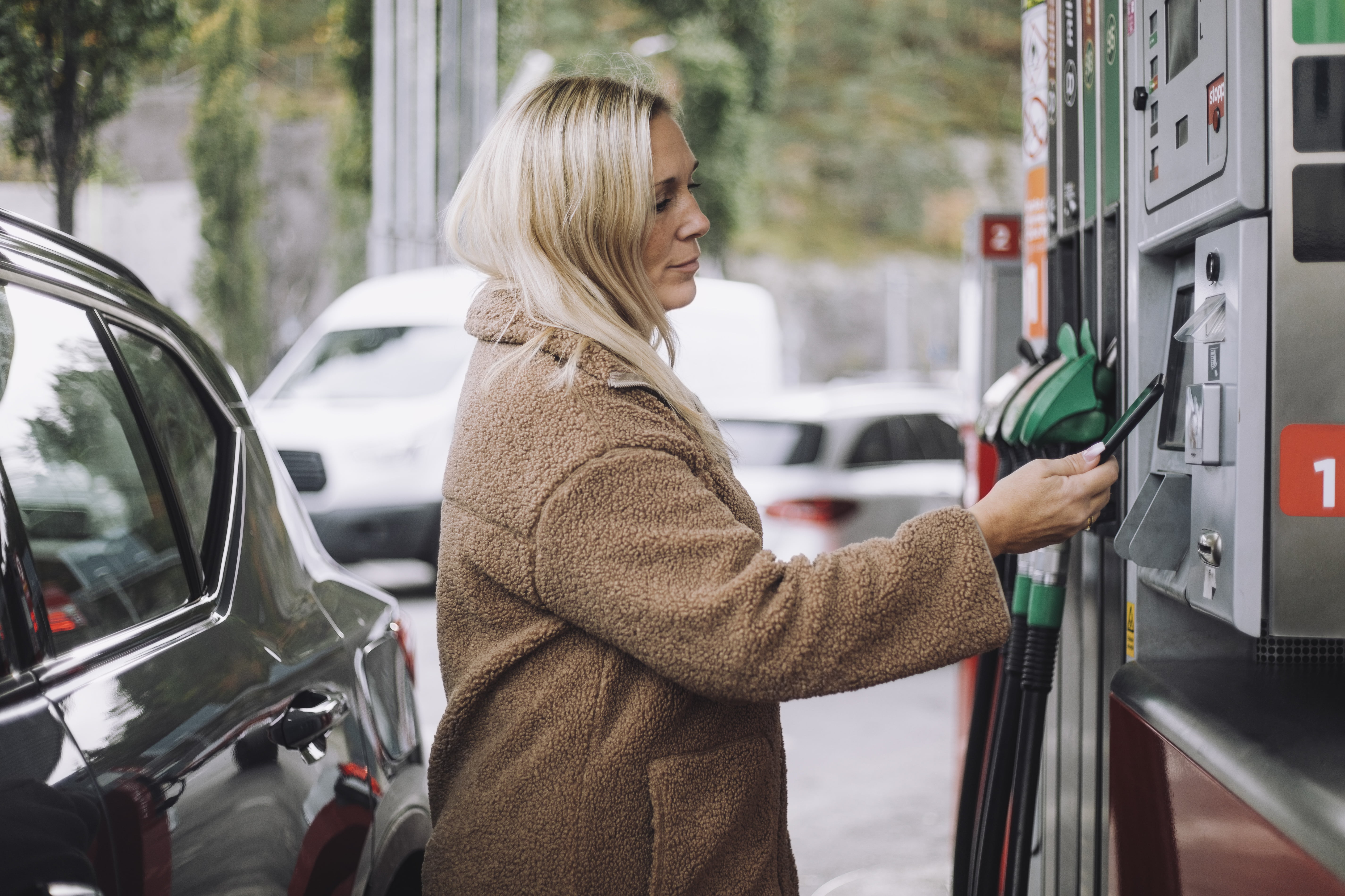 Dame som betaler med mobilen på bensinstasjon