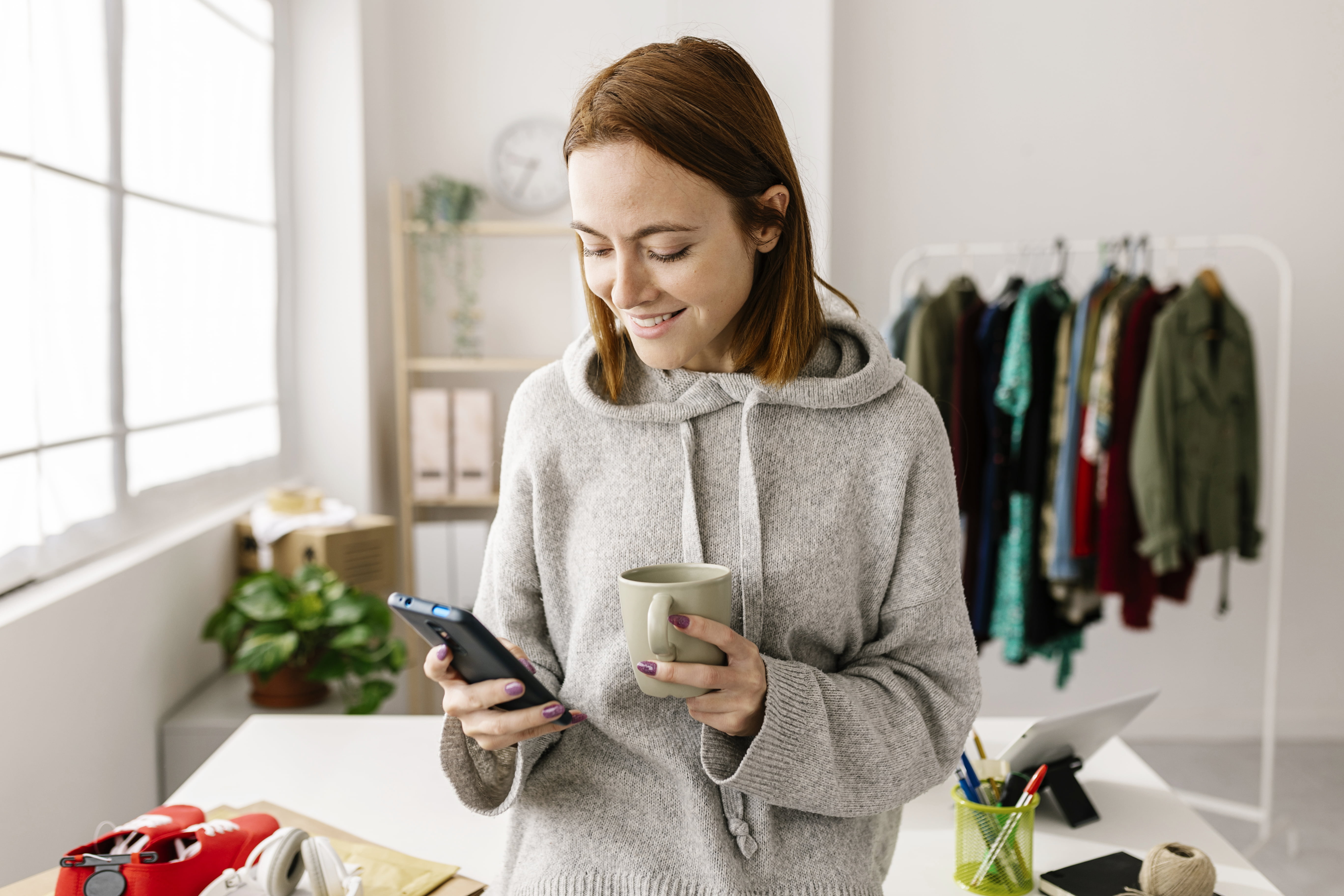 Jente med kaffe i hånden, som ser på mobilen sin