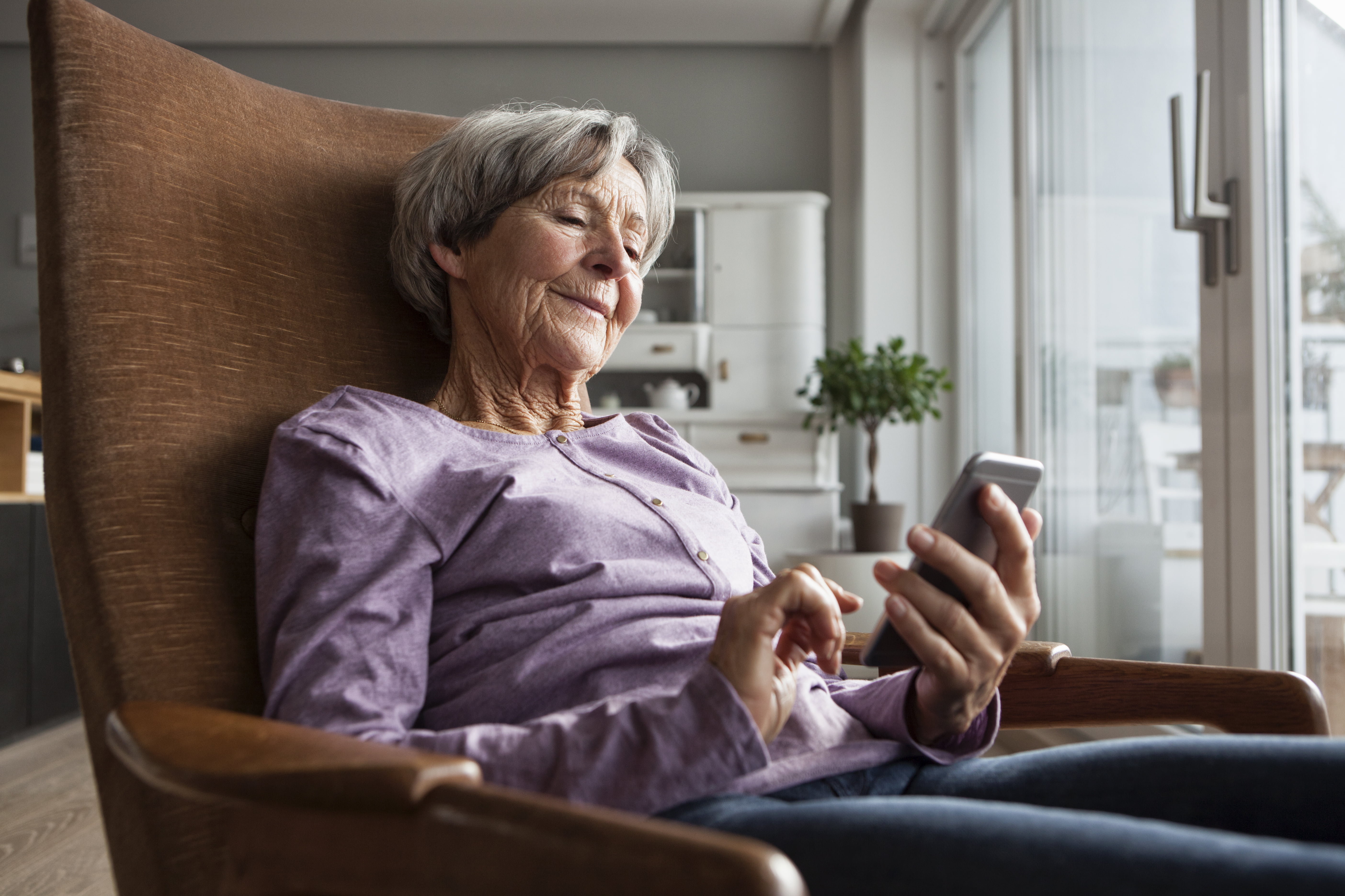 En eldre dame som sitter i en stol og skriver sms