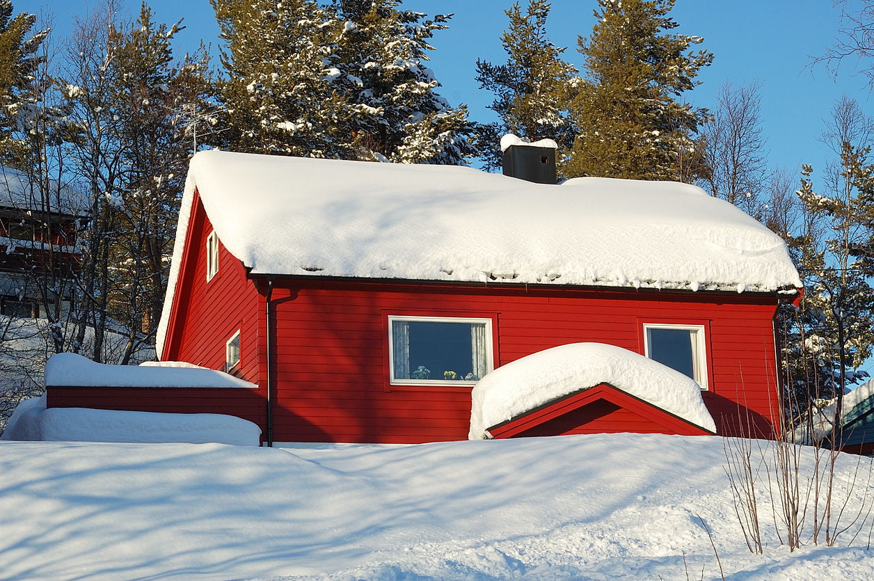 Et rødt hus som er dekket med snø