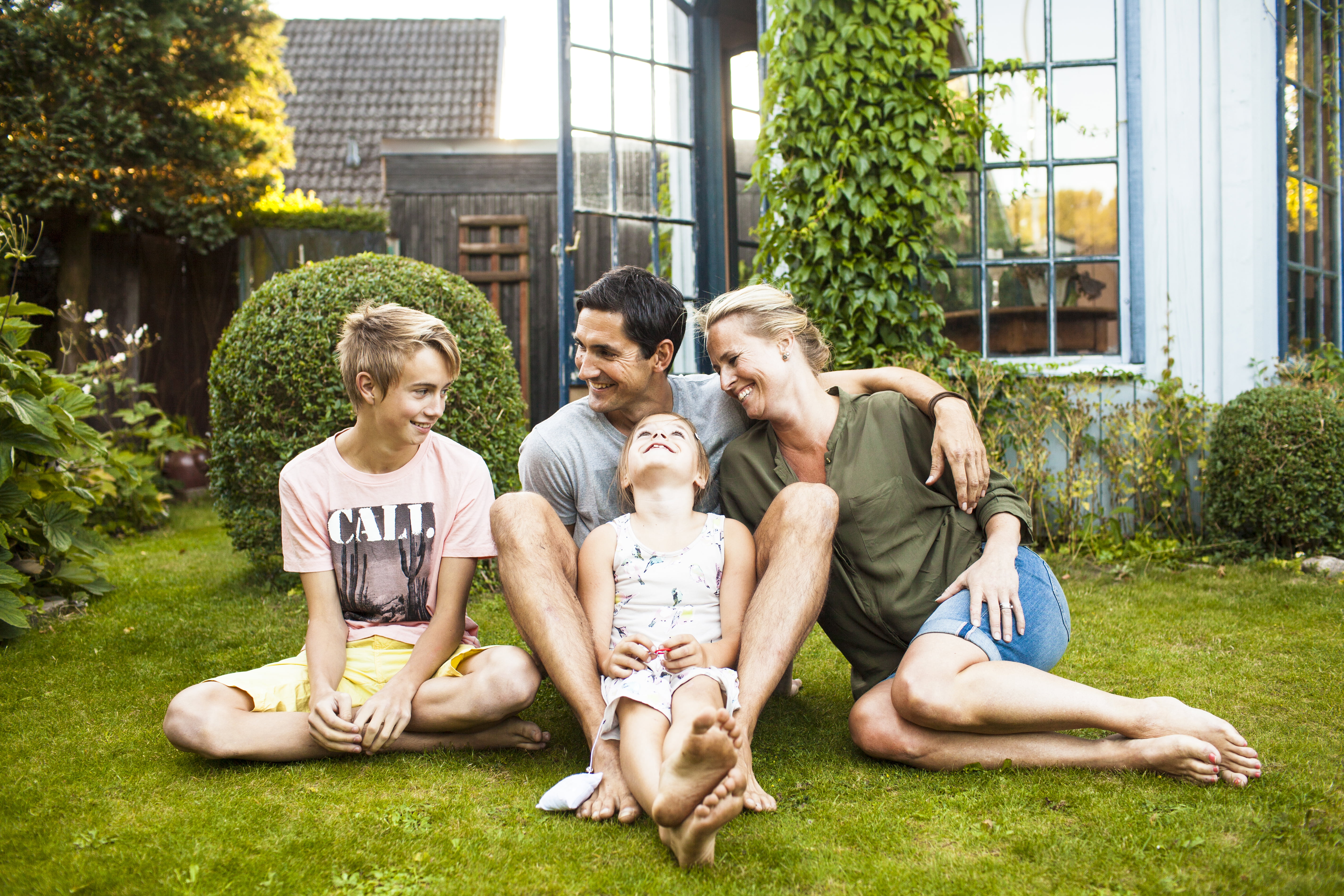 Familie med to barn som sitter på gresset ute i hagen en sommerkveld