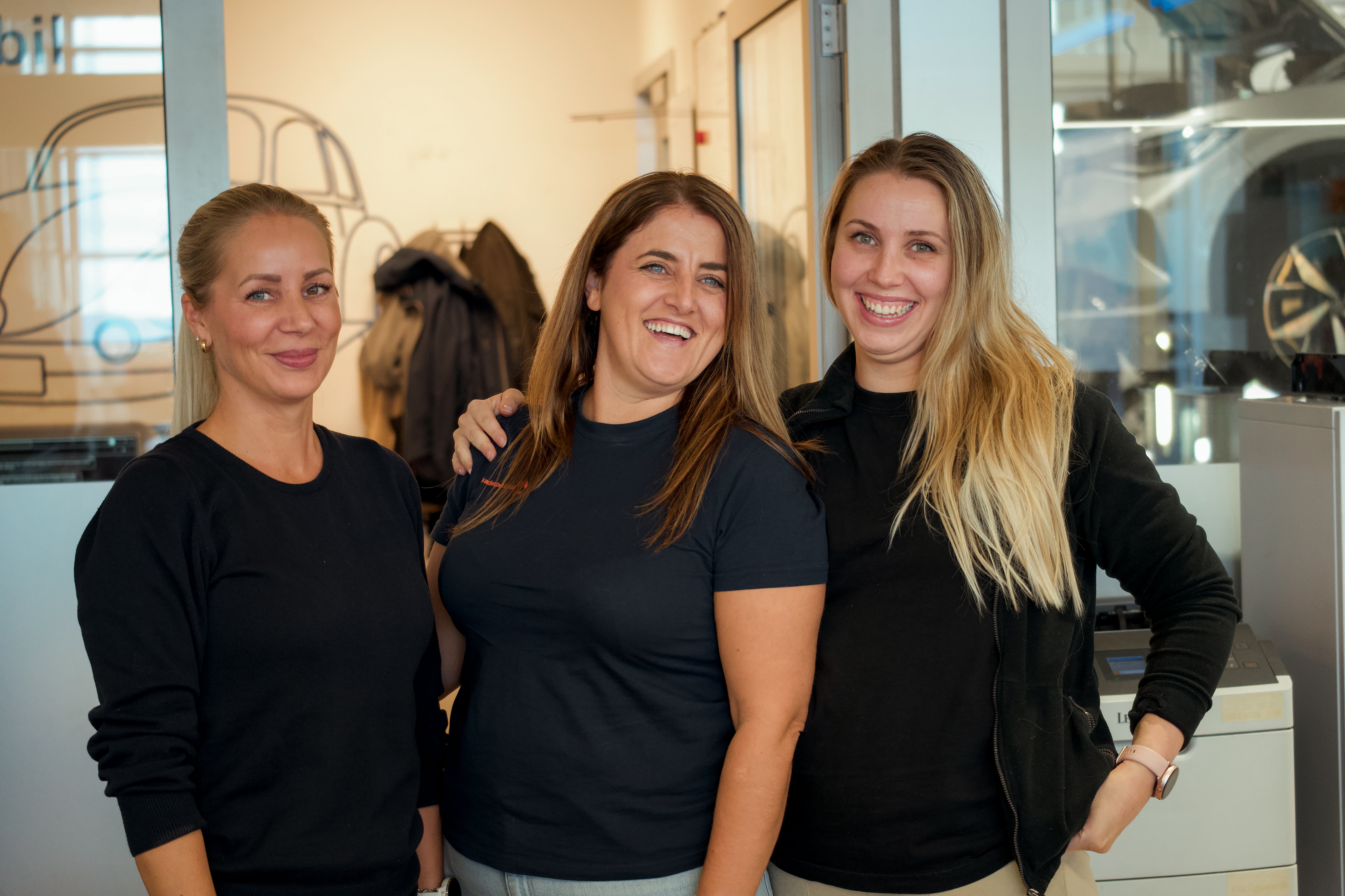 3 smilende damer i et bilverksted